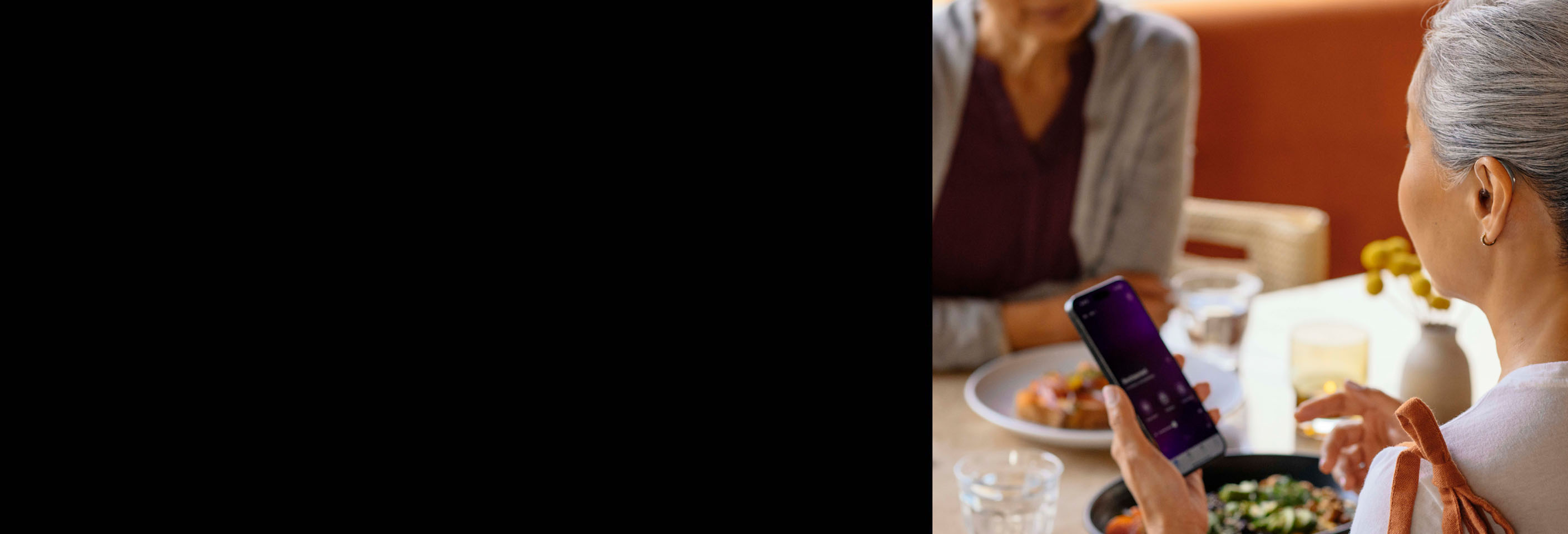 A woman wearing hearing aids using her phone app while talking to another woman at a restaurant